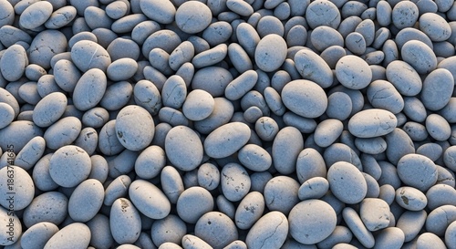 Close-up of smooth rounded pebbles and stones on a natural beach surface with soft shadows and subtle color variations for a tranquil coastal scene