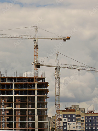Tower cranes work during the construction of a multi-story building. New apartments for residents and premises for offices. Risky work at height. Lifting heavy building materials. City development