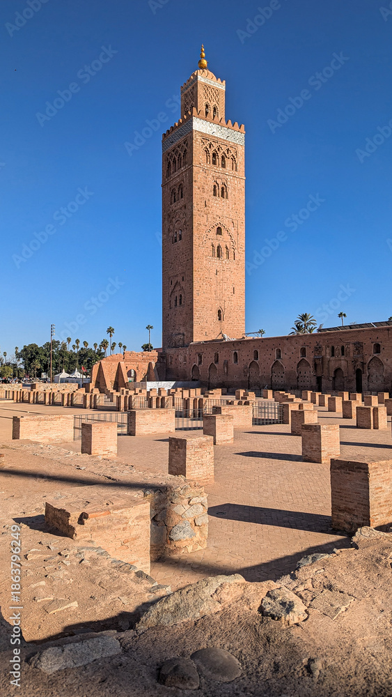 Fototapeta premium Koutoubia-Moschee in Marrakesch: Das markante Minarett aus rötlichem Sandstein erhebt sich vor tiefblauem Himmel über die historische Altstadt. 
