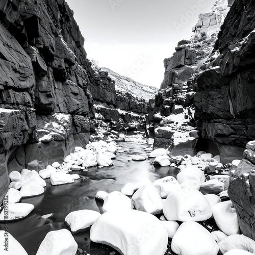 Black and white photograph of a deep, rocky canyon with a flowing river and snow