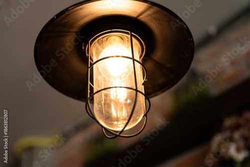 A classic style ceiling lighting lamp with iron cage during it glowing in warmlight shade. Interior object, close-up with selective focus.