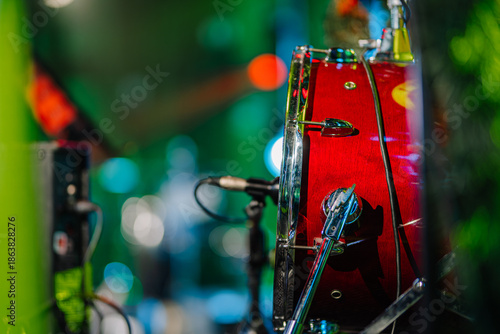 Close-up view of a vibrant red drum set with shiny chrome hardware, surrounded by colorful stage lights, capturing the energy of a live music performance atmosphere