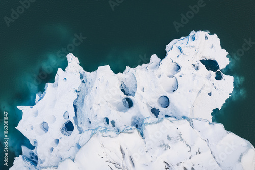 Aerial view of a colossal, porous iceberg, its stark white form contrasting dramatically against the deep turquoise waters, creating an otherworldly spectacle, Southern Iceland, Iceland.