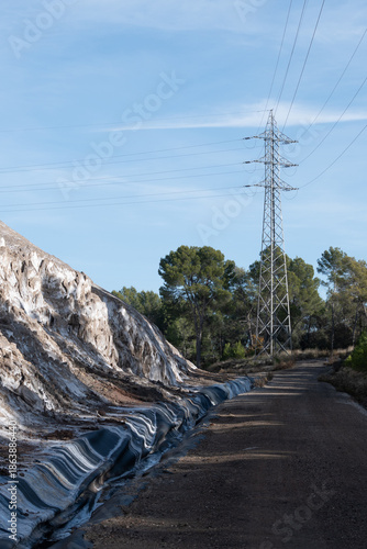 Vast industrial salt mountain looms beside a power line pylon, symbolizing immense resources, environmental challenges, and sustainable solutions. 