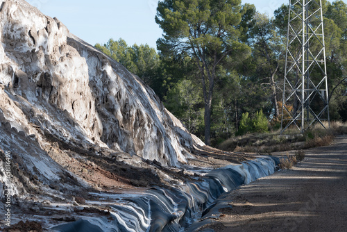 A striking view of an arid landscape dominated by a dramatic slope covered in white and grey mineral efflorescence, resembling salt or gypsum deposits. 
