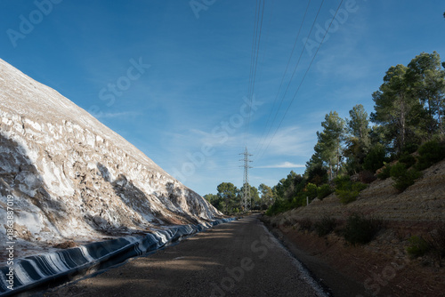 Vast industrial salt mountain looms beside a power line pylon, symbolizing immense resources, environmental challenges, and sustainable solutions. 