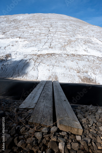 Massive white salt mountain under blue sky, viewed from weathered wooden planks. Symbolizes raw natural resources, grand challenges, aspiration, and a unique perspective on the journey ahead.