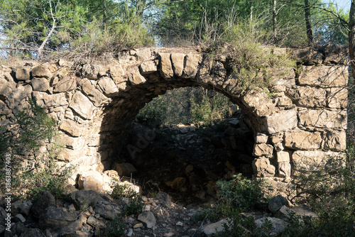 Ancient stone archway in a sun-dappled forest, forming a rustic passage. 