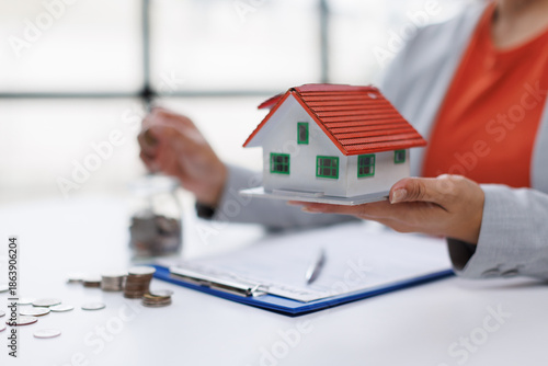 Investing real estate growth. Real estate asset property. Mortgage residential finance. Real estate investment. A woman is sitting at a desk with a laptop and a miniature house model.

