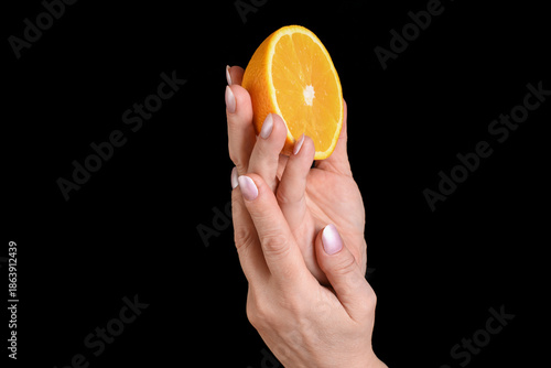 A female hand holding a fresh half orange on a black background. Minimal studio close-up suitable for food, natural ingredients, skincare, hand care, beauty, and wellness concepts.