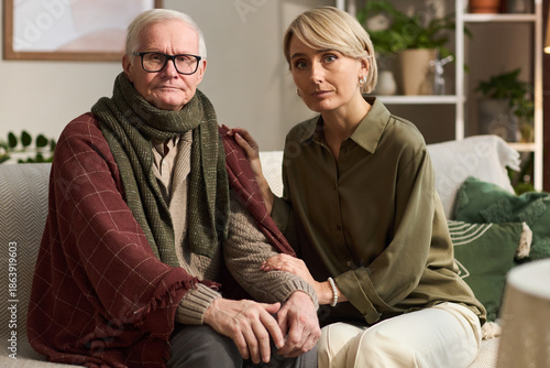 Wallpaper Mural Senior Caucasian man sitting on sofa with middle aged adult daugther supporting him, both looking at camera, hands gently touching, indoor setting with plants in background Torontodigital.ca