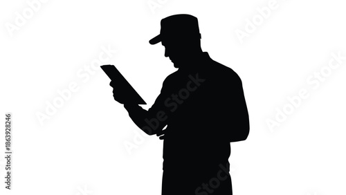 Silhouette of construction worker wearing a baseball cap reading information on a digital tablet device