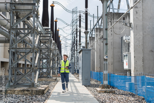 Foto Professional electrical engineer walking and inspecting high voltage equipment at power substation, monitoring energy infrastructure for industrial system maintenance and grid reliability