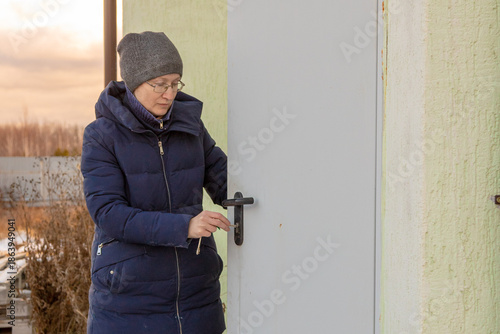 Woman in warm clothing unlocking a door with a key. Preparing to enter her country house during colder weather.