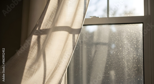 Sunlit sheer curtain gently blowing by a window with visible dust particles