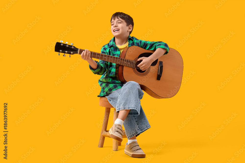 Naklejka premium Cute boy playing guitar on yellow background