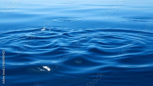 Mesmerizing closeup of crystal clear water droplets gracefully falling and creating intricate ripples and splashes on a serene deep blue liquid surface showcasing the dynamic beauty and purity of wat.