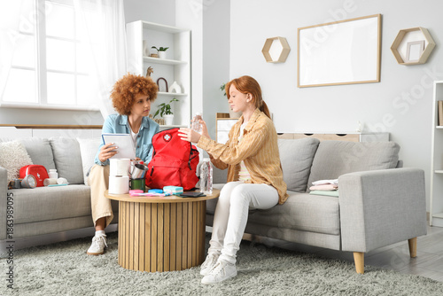 Redhead mother with check-list and her teenage daughter packing emergency bac...