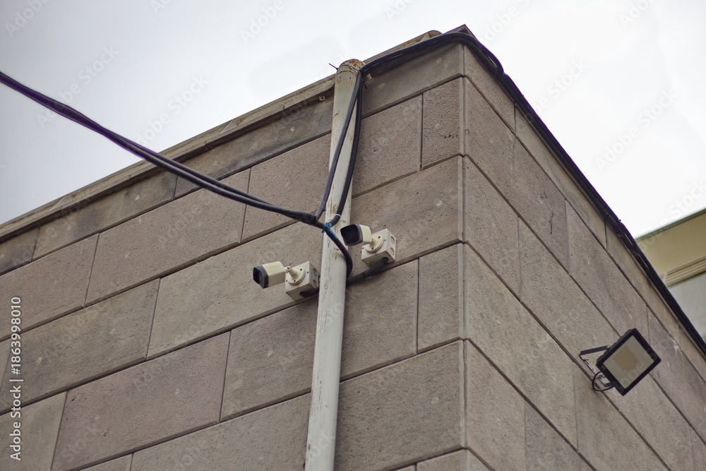 Obraz premium Two CCTV cameras on the building's facade. Close-up of the cameras against a brick wall. Smart city concept. City safety and security.