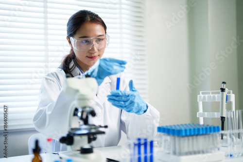 Asian adult female scientist researcher conducts experiment holds test tube chemical analysis professionally carefully with focus modern laboratory medical science facility