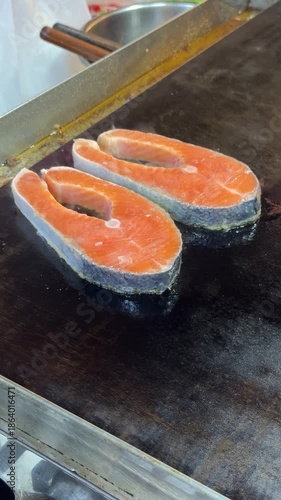 Two pieces of salmon are on a grill. The salmon is cooked and has a nice sear. The grill is black and shiny