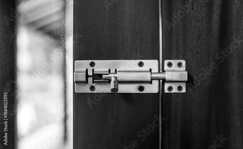 A close-up shot of a silver metal sliding barrel bolt lock installed on a dark wooden door, showing the security hardware in a locked position
