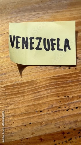 Handwritten Word Venezuela on Yellow Sticky Note over Wooden Background