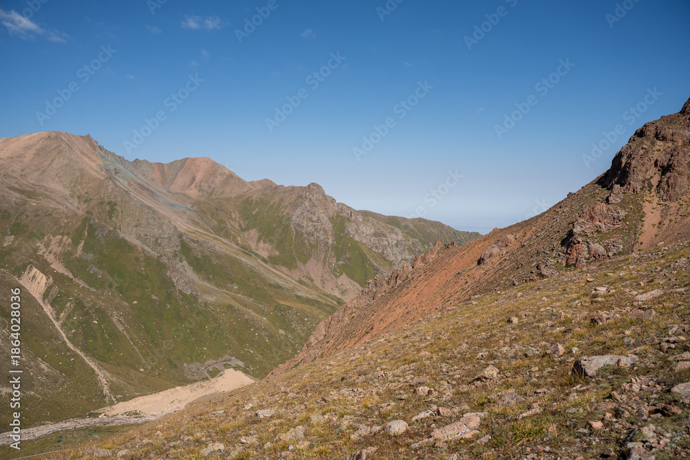 Fototapeta premium Winding gravel road in the high mountains of Tien Shan with a view of the massive Tuyuksu glacier. Remote alpine landscape in Central Asia