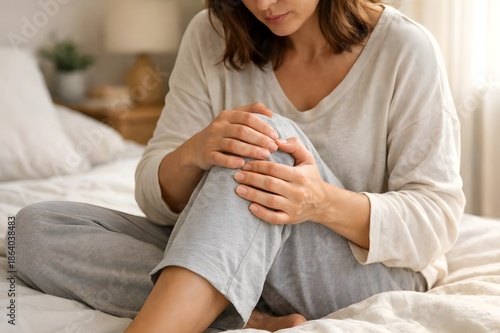 Woman sitting on bed and massaging her painful knee joint