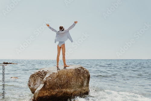 Woman Sea Rock, arms outstretched, embracing freedom on coastal rock under sunny sky.