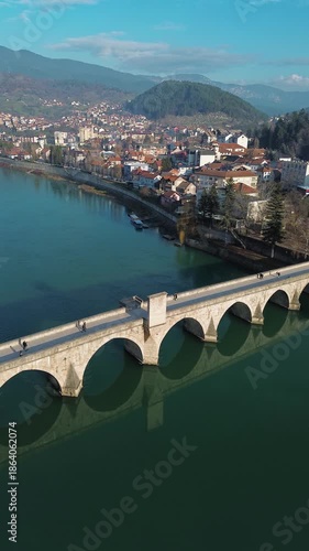 Aerial view of the historic Mehmed Pasha Sokolovic Bridge crossing the Drina River in Visegrad, Bosnia and Herzegovina. Timeless Ottoman architecture meets calm river landscape