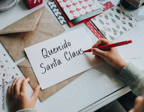 Niño escribiendo carta a Papá Noel en mesa con sobre y material escolar