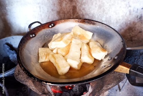Cassava is being fried in a pan over a charcoal stove.