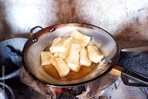 Cassava is being fried in a pan over a charcoal stove.