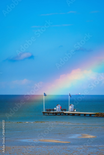 A wooden walkway of a pier on the Baltic Sea with two changing rooms and a rainbow.