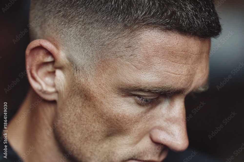 Obraz premium Man looking down, showing a modern faded haircut and a thoughtful expression