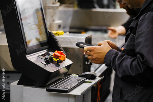 Factory technician using data collection device to log operations on CNC control console with digital display and manual controls