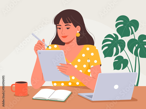 A young woman dressed in a polka dot dress sits at a table, focused on her tablet while a laptop is open nearby, creating an atmosphere of creativity and productivity.