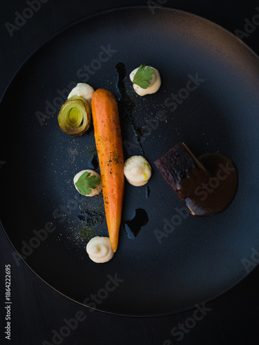 Slow cooked pork belly with celeriac puree, glazed carrot and leek served in fine dining gourmet food restaurant. Black plate on black background. Art of Plating