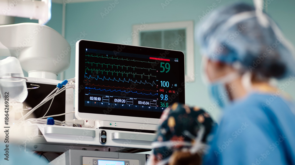 Fototapeta premium Surgical team monitors patient vitals on advanced medical equipment in a sterile operating room, showcasing high-tech healthcare environment and professional teamwork