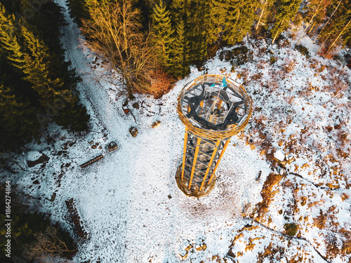 Visitors stand at the top of Svetly vrch lookout tower in Albrechtice. The ground is covered with snow, and the surrounding trees are bare. The scene captures winter in the mountains.