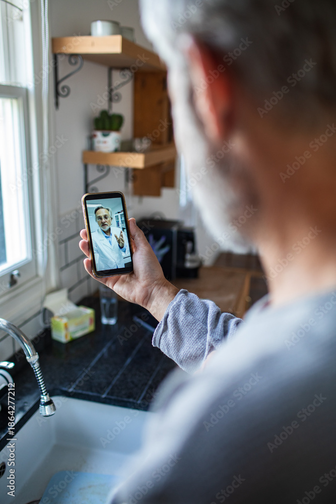 Fototapeta premium Mature man focused on telehealth video call with doctor in home kitchen