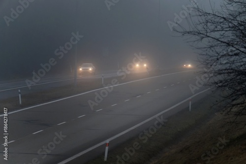 Car traveling on the foggy road with headlights or headlamps on. Low visibility - Dangerous driving of cars in winter in bad weather.