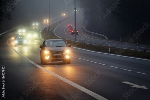 Car traveling on the foggy road with headlights or headlamps on. Low visibility - Dangerous driving of cars in winter in bad weather
