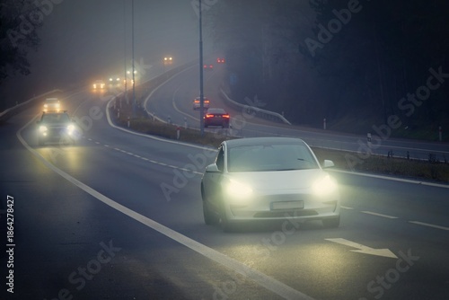 Bright headlights of a car driving on foggy winter road