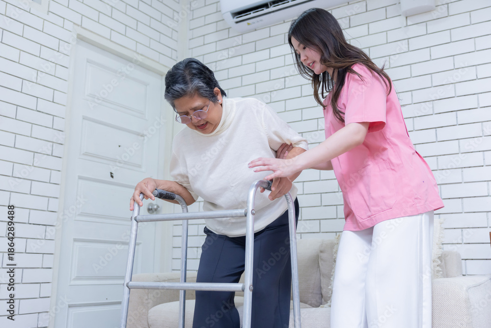 Fototapeta premium A young woman assists an elderly woman using a walker in a room