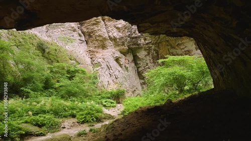 A view inside the Devetashka Cave near Devetaki village and the Osam river in Lovech, Bulgaria. This massive open-air cave features natural light streaming through large ceiling holes, illuminating th
