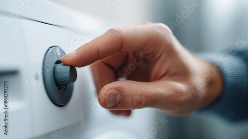 Close-up of hand adjusting black control knob on white appliance with blurred background