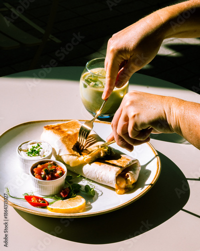 Hands cutting into breakfast burrito with drastic shadows.