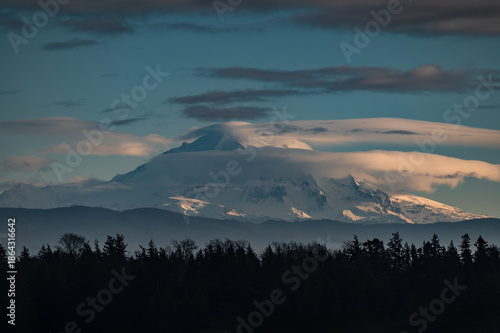 Dramatic clouds surround the magnificent volcanic mountain called Mt. Baker located in the Cascade range. The Cascade range a major mountain system in western North America, stretching over 700 miles.